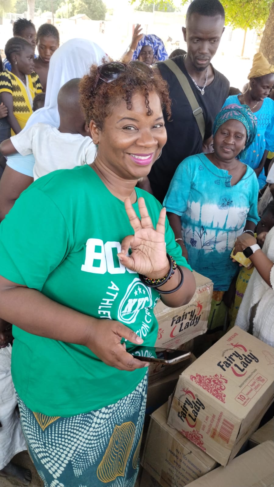 Gigi smiling with community members beside boxes of donated menstrual supplies